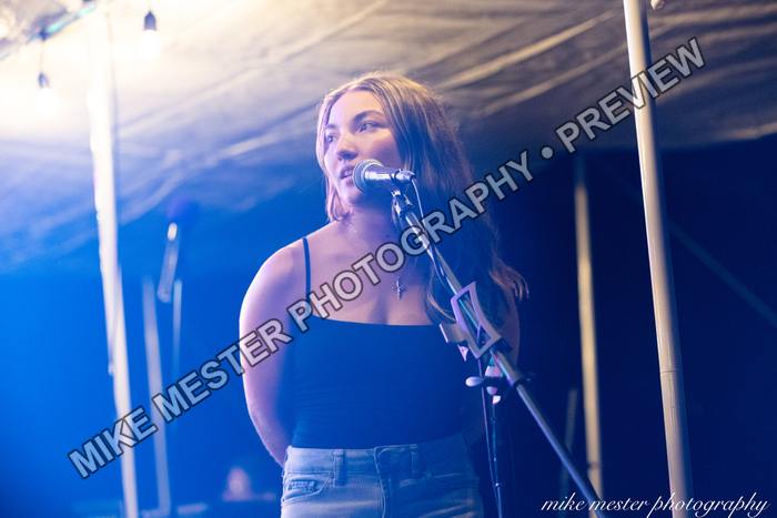 Female vocalist singing on an outdoor stage under blue light.