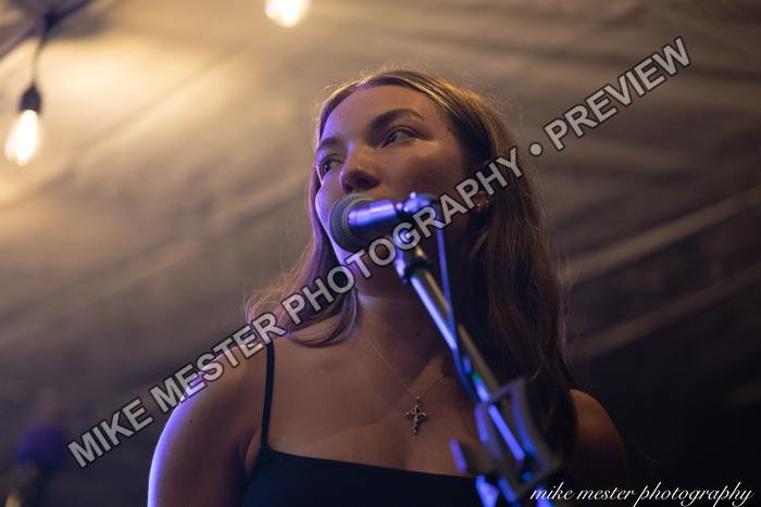 Female vocalist at a microphone beneath warm string lights.