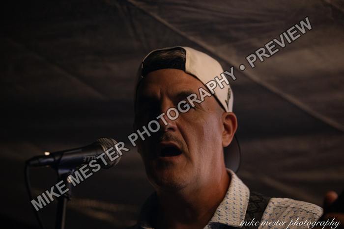 Bass guitarist singing into a microphone beneath the stage canopy.
