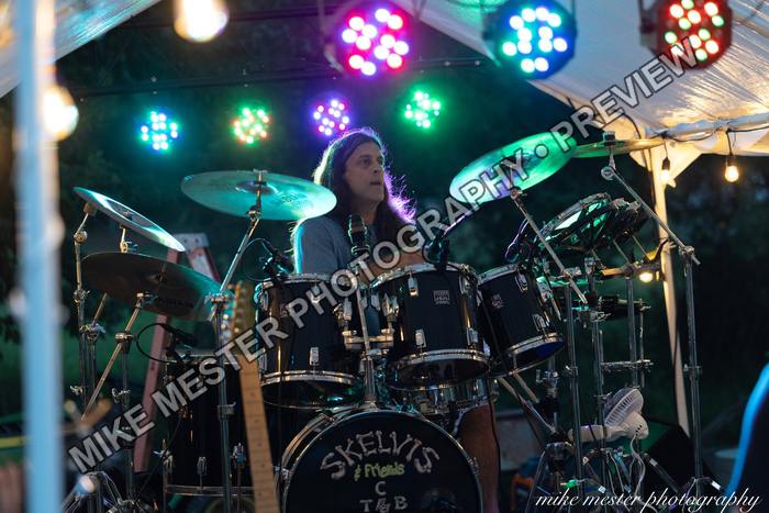 Drummer performing behind a full kit under colorful lights.