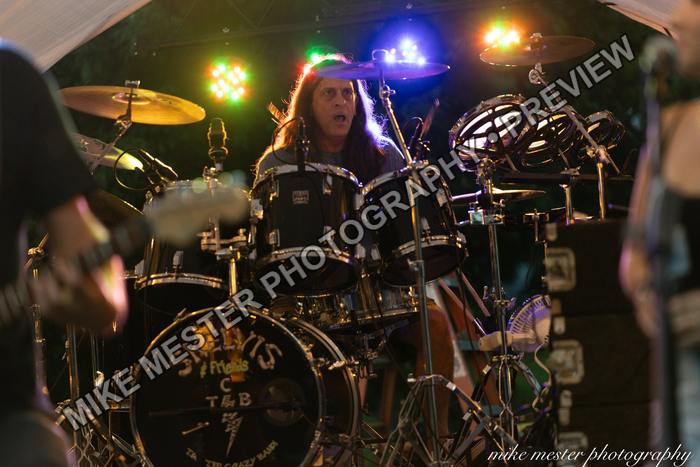 Drummer performing beneath bright green, blue, and amber lights.