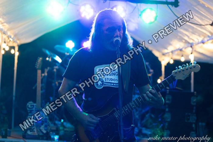 Bearded guitarist performing in vivid blue stage light.