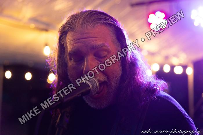Long-haired vocalist singing beneath warm purple stage light.