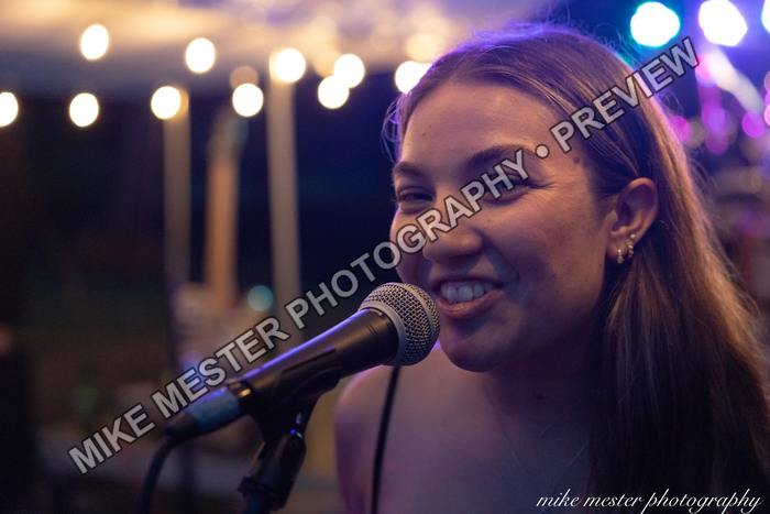 Female vocalist smiling at a microphone with colorful lights behind her.