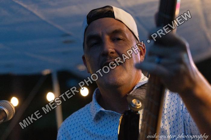 Bass guitarist singing into a microphone beneath the dark stage canopy.