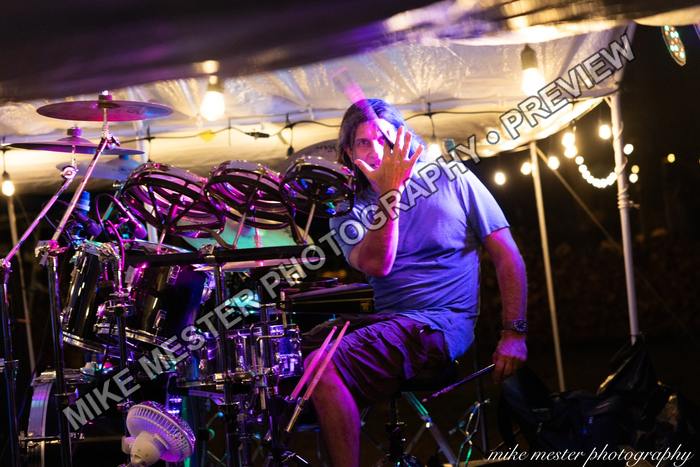 Drummer performing behind a large kit beneath purple stage light.